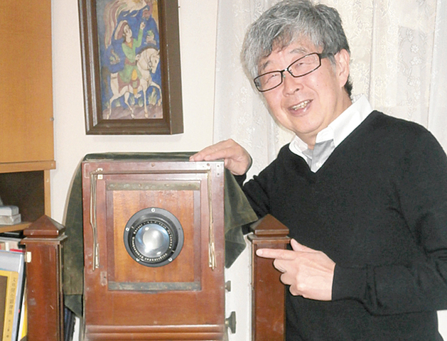 息子の敬章さん。指差しているのは、 父親もコレクションしていたという木製国産写真機。